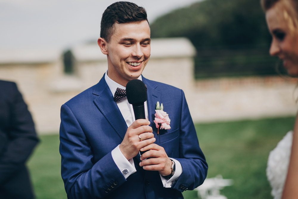 a groom speaking into a microphone at an outdoor wedding ceremony