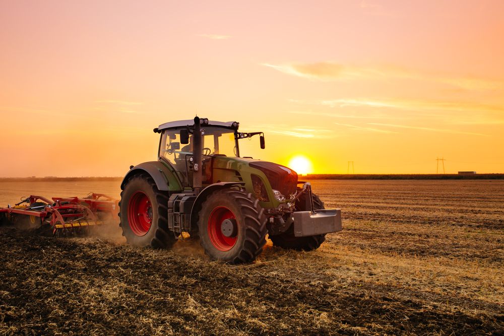 a tractor plowing on a farm at sunset