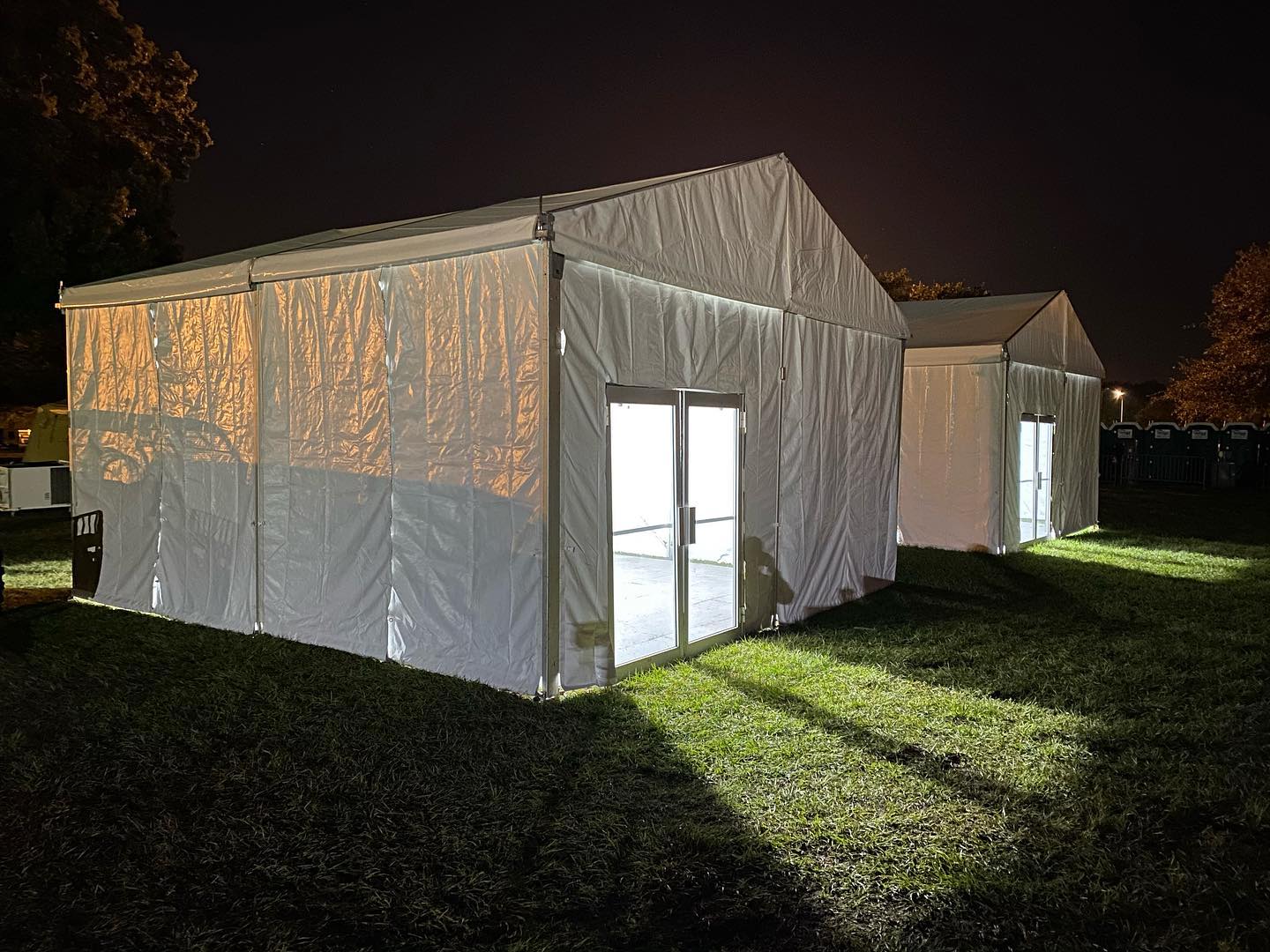 Large white tents with glass doors sit on a dark field.