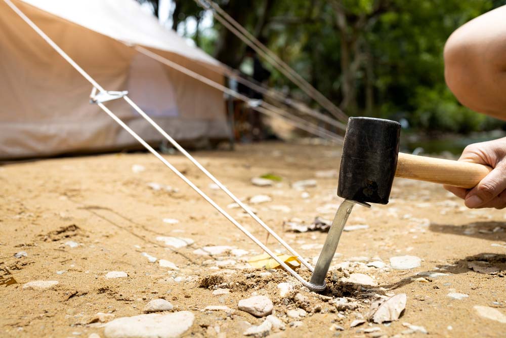 a person hammering in a tent stake to support an event tent in windy conditions