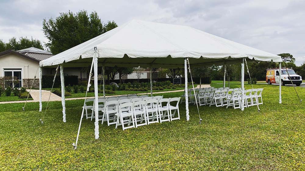 A white outdoor tent on a grassy area with white chairs in rows facing in the same direction.