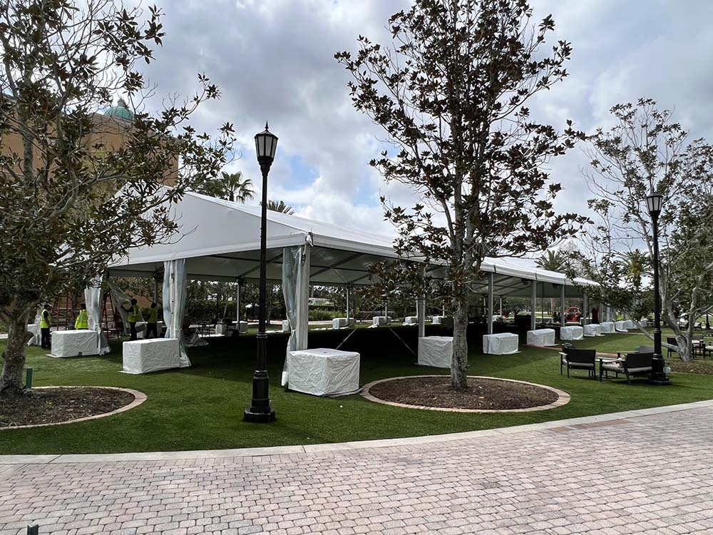 An outdoor white tent on a grassy area outside a building and stone walkway.