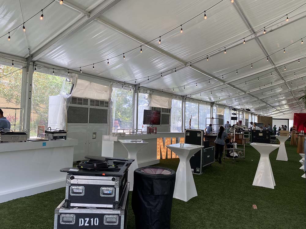 Interior of an outdoor tent with a grass floor, cocktail tables, and string lights.