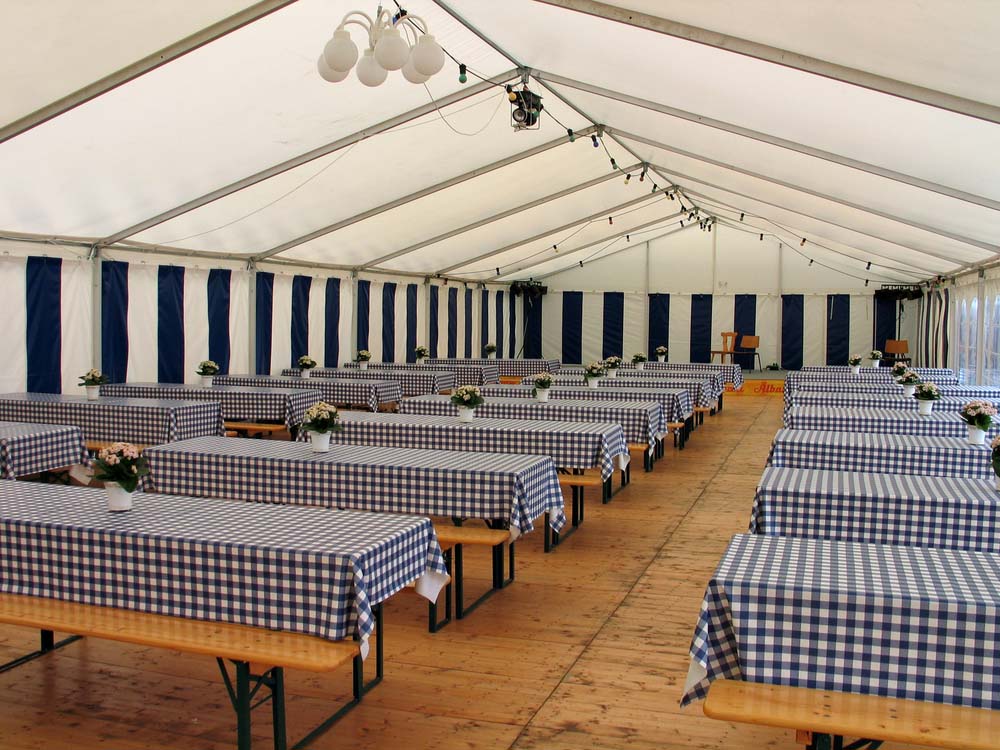The interior of a walled tent with long tables covered in blue gingham tablecloths.