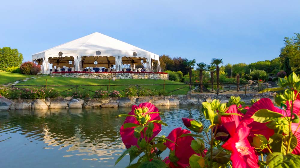 an event tent set up next to a lake with flowers in the foreground