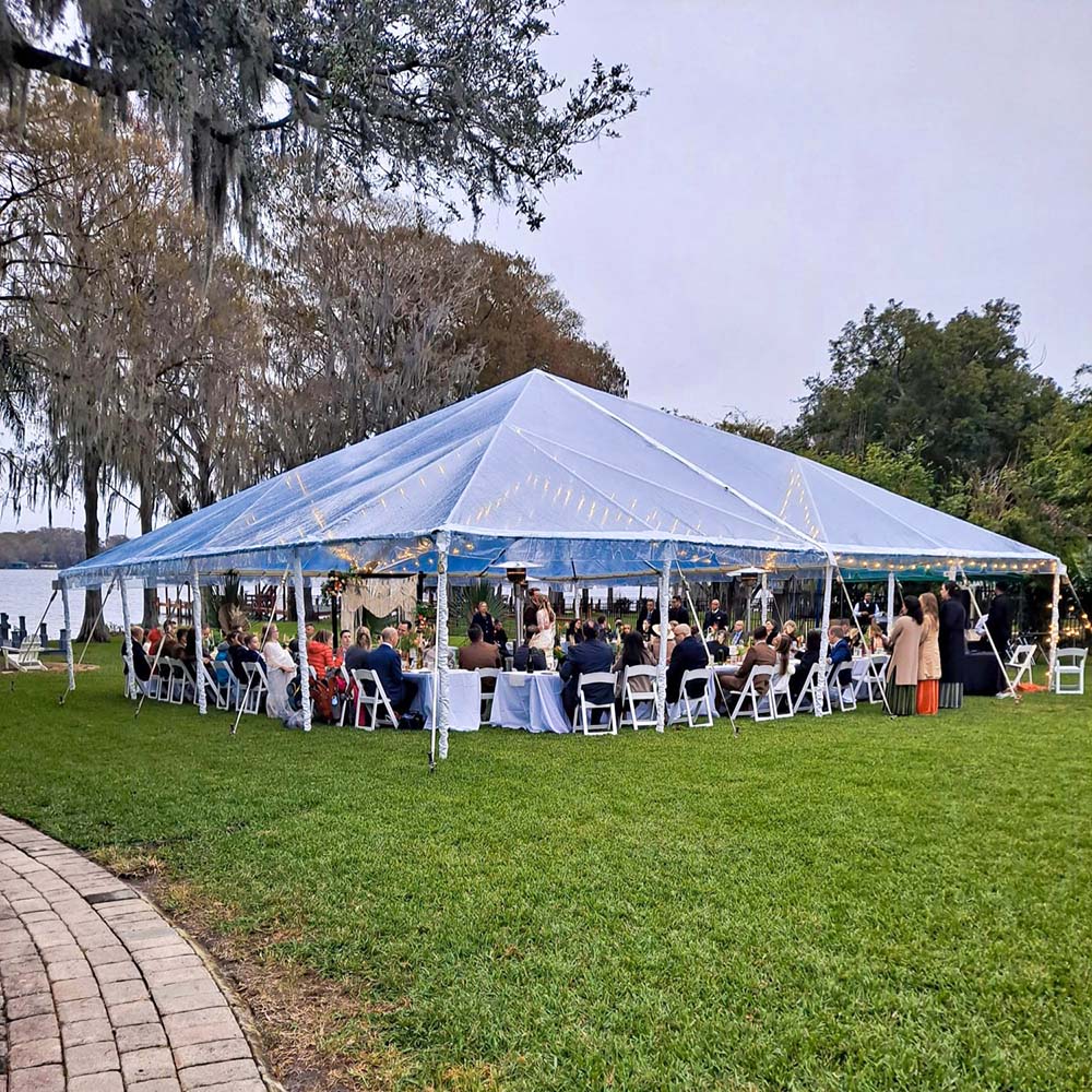 An outdoor wedding with a light blue tent with strings of yellow lights on the inside.