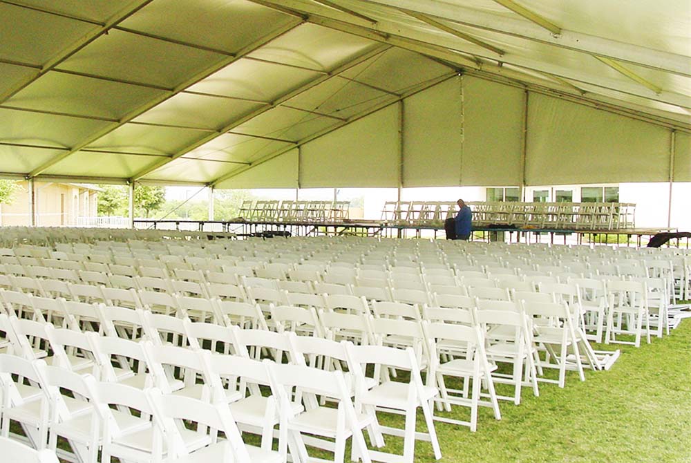 Rows of white chairs underneath an outdoor tent for a church event