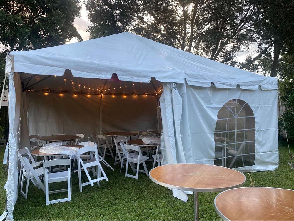 A medium-sized outdoor tent featuring tent sides, white chairs, brown tables, and orange string lights