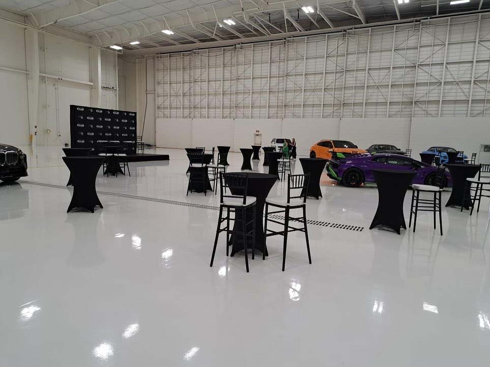 rental tables and chairs in a hangar in front of luxury cars