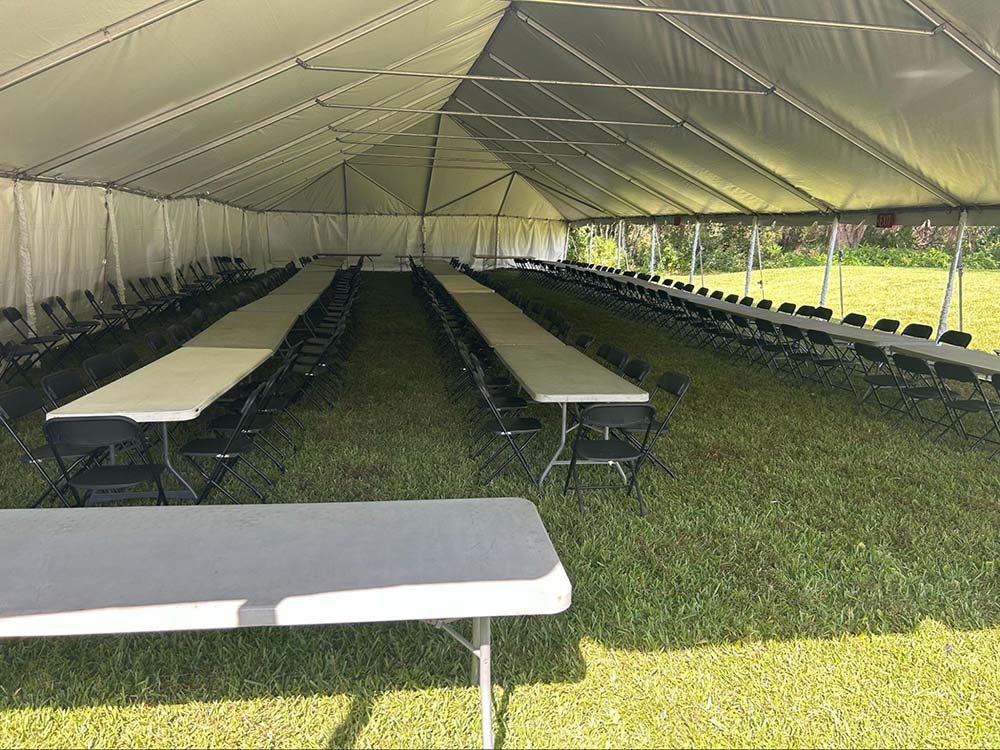 A large outdoor tent with long, white tables aligned with black folding chairs